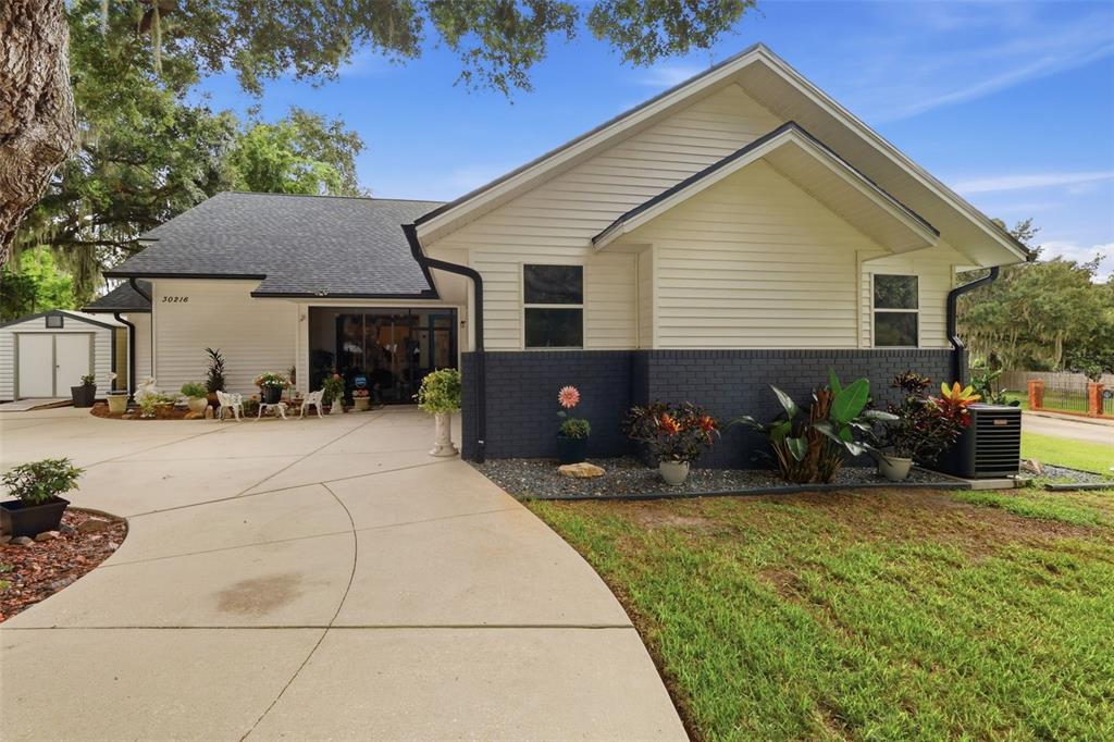 A single-story house with white siding, a dark brick base, and a concrete driveway — 30216 HARRIS DRIVE, LEESBURG, FL