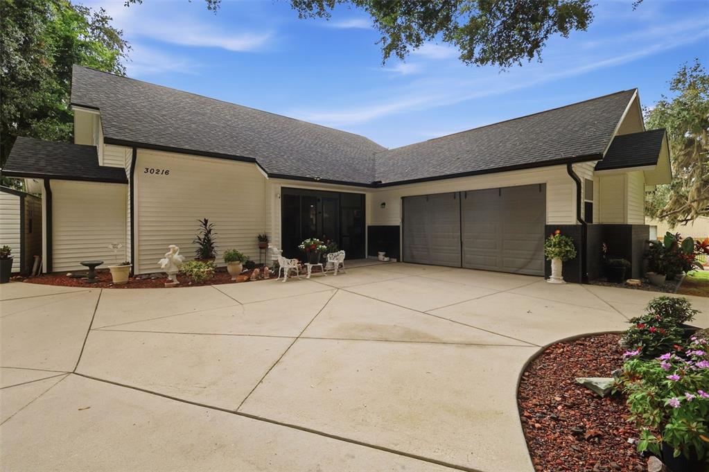 A single-story house with white siding, a dark shingled roof, and a concrete driveway — 30216 HARRIS DRIVE, LEESBURG, FL