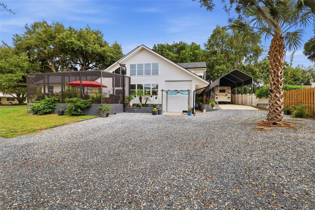 A white house with a screened-in porch, gravel driveway, and a covered RV parking area — 30216 HARRIS DRIVE, LEESBURG, FL