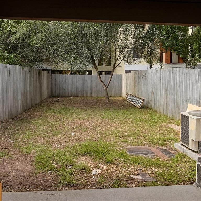 A fenced-in backyard features a patch of grass, a single tree, and an air conditioner — 2772 GRAY FOX LANE, ORLANDO, FL