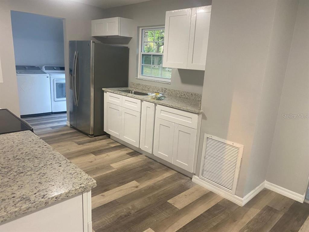 A kitchen features white cabinets, granite countertops, stainless steel appliances, and wood-look flooring — 473 LAKE ROAD, OCALA, FL
