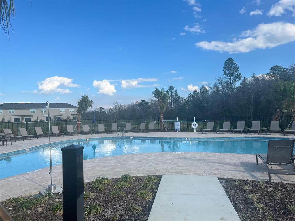 A swimming pool with lounge chairs on a paved deck under a blue sky — 2073 VIEWFINDER STREET, KISSIMMEE, FL