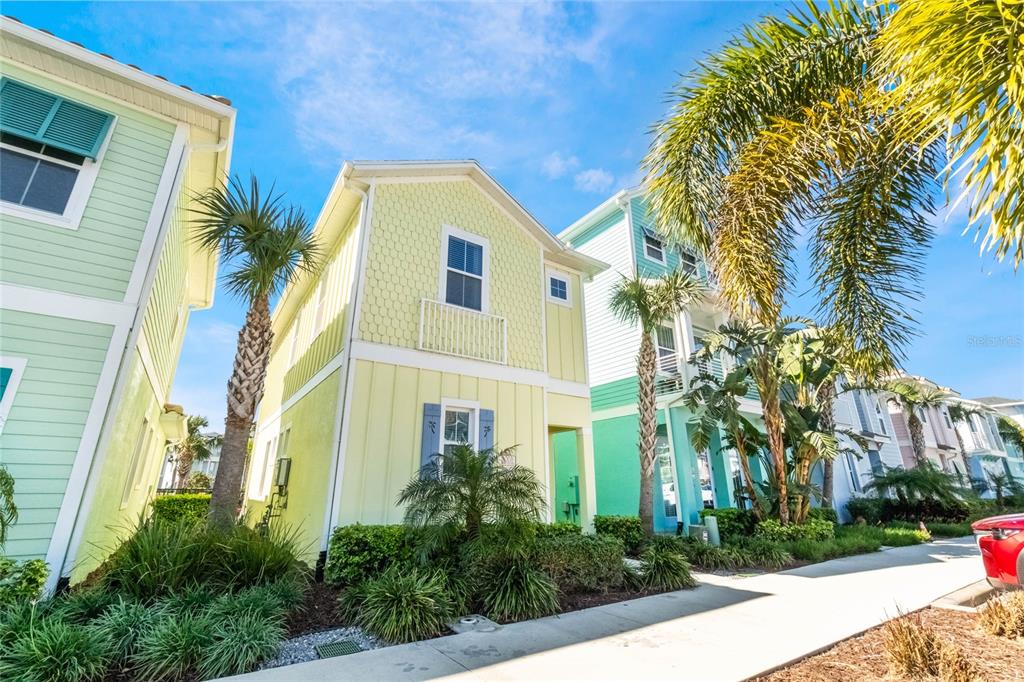 A light yellow two-story house with blue shutters stands next to palm trees and sidewalks — 8008 SANDY TOES WAY, KISSIMMEE, FL