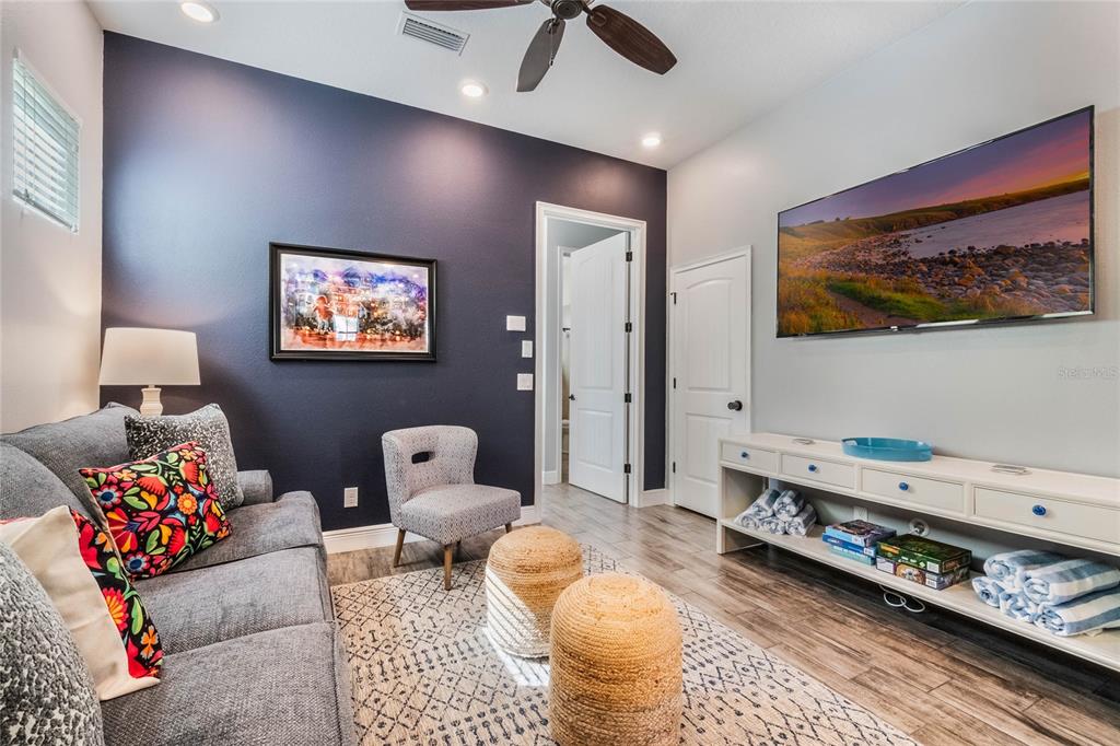 A living room features a dark blue accent wall, gray sofa, television, and wood flooring — 8008 SANDY TOES WAY, KISSIMMEE, FL