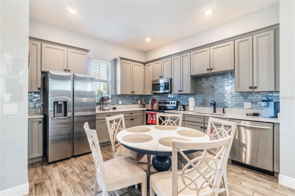 A kitchen features gray cabinets, stainless steel appliances, a blue tile backsplash, and a dining table — 8008 SANDY TOES WAY, KISSIMMEE, FL