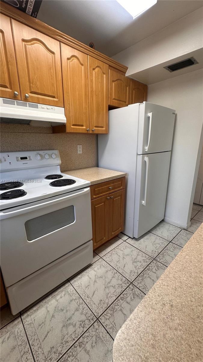 A kitchen features wood cabinets, white appliances, a tiled floor, and beige countertops — MIAMI BEACH, FL