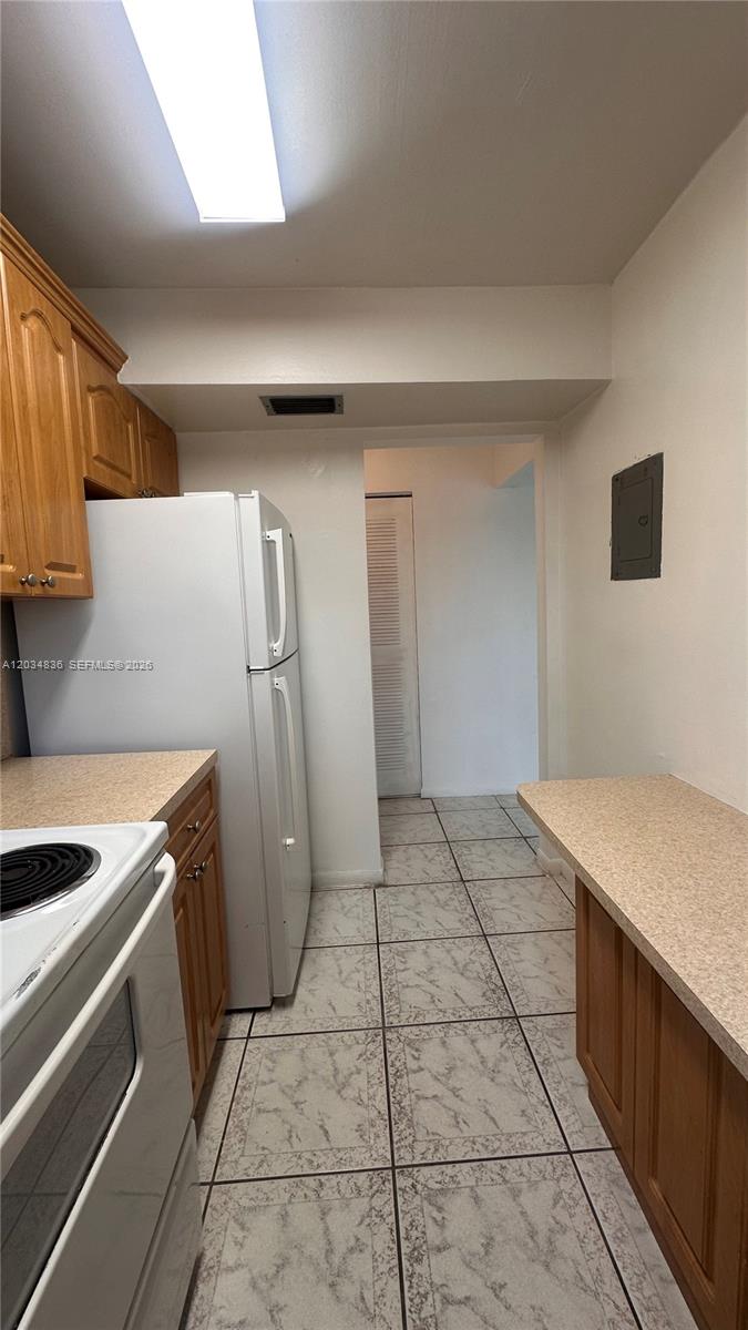 A kitchen features light wood cabinets, beige countertops, white appliances, and light-colored tiled flooring — MIAMI BEACH, FL