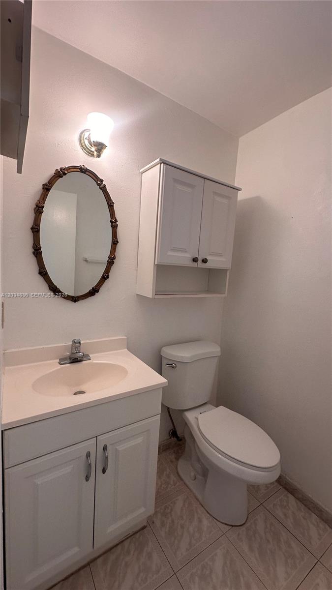 A bathroom features a white vanity with a sink, a toilet, and a wall-mounted cabinet — MIAMI BEACH, FL