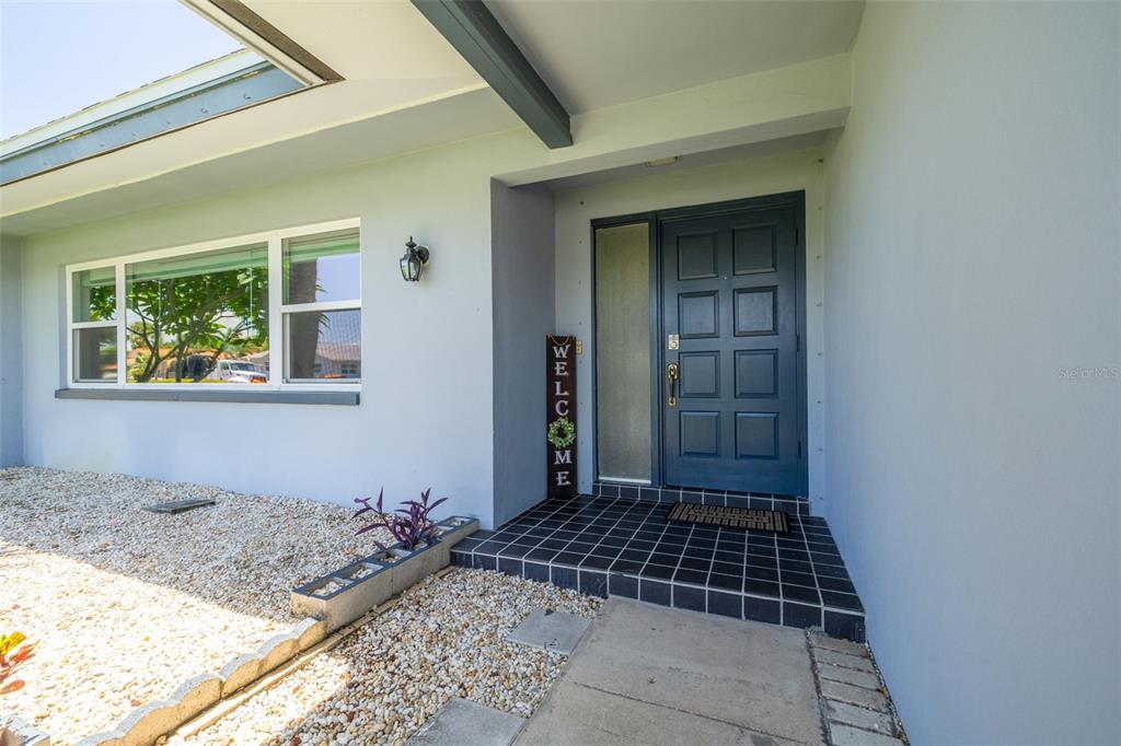 A blue front door with a sidelight sits under a covered entryway next to a window — 8960 140TH STREET, SEMINOLE, FL