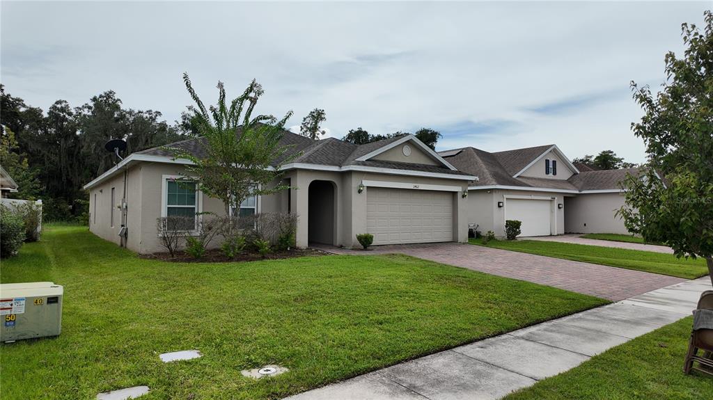 A single-story suburban house with a tan stucco exterior, a two-car garage, and a lawn — 2462 ADDISON CREEK DRIVE, KISSIMMEE, FL