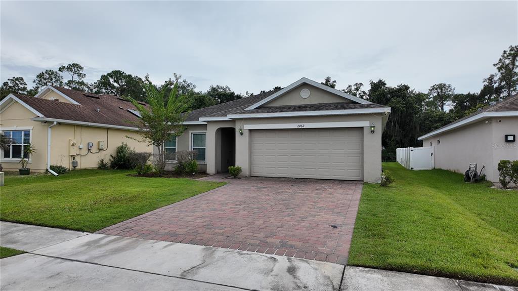 A single-story house with a brick paver driveway, a two-car garage, and a green lawn — 2462 ADDISON CREEK DRIVE, KISSIMMEE, FL