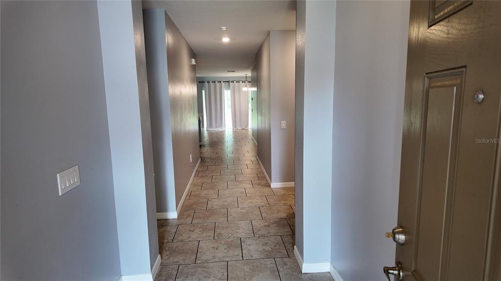A tiled entryway leads down a hallway toward a living area with white curtains — 2462 ADDISON CREEK DRIVE, KISSIMMEE, FL