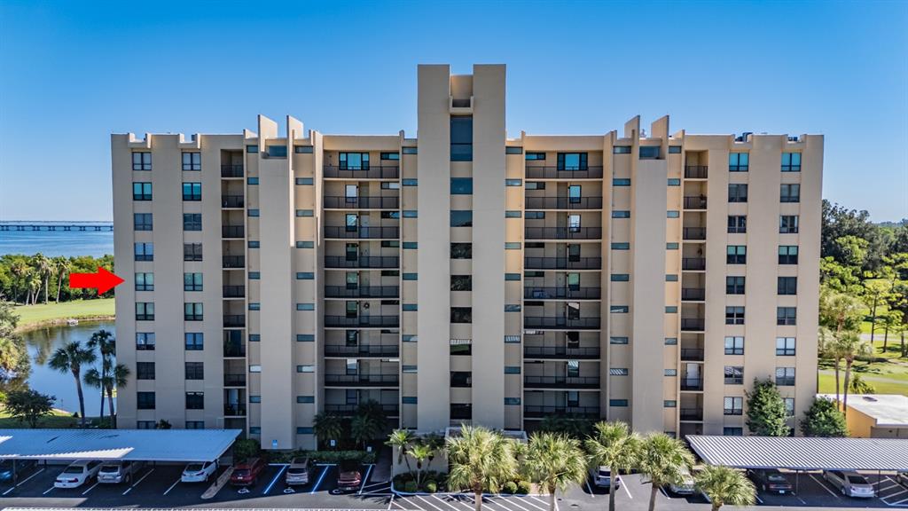 An exterior view of a multi-story apartment building with a red arrow pointing toward a window — 2620 COVE CAY DRIVE UNIT 601, CLEARWATER, FL