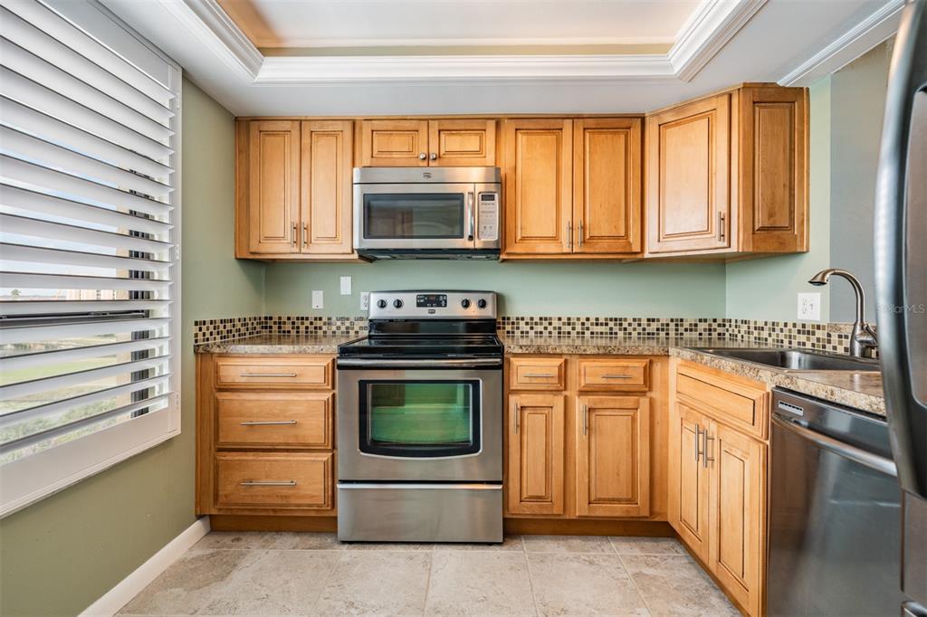 A kitchen with light wood cabinets, stainless steel appliances, granite countertops, and a tiled backsplash — 2620 COVE CAY DRIVE UNIT 601, CLEARWATER, FL