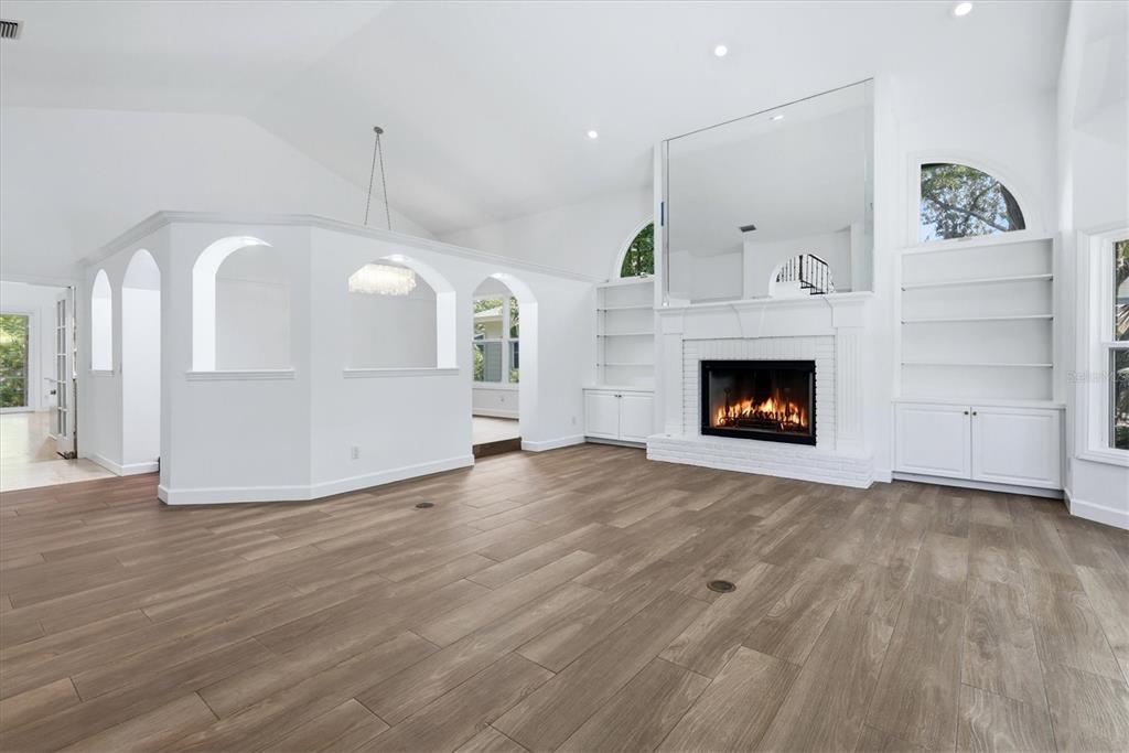 A spacious living room features wood-look tile flooring, a white fireplace, and built-in shelving — 1351 DIXIE LEE LANE, SARASOTA, FL