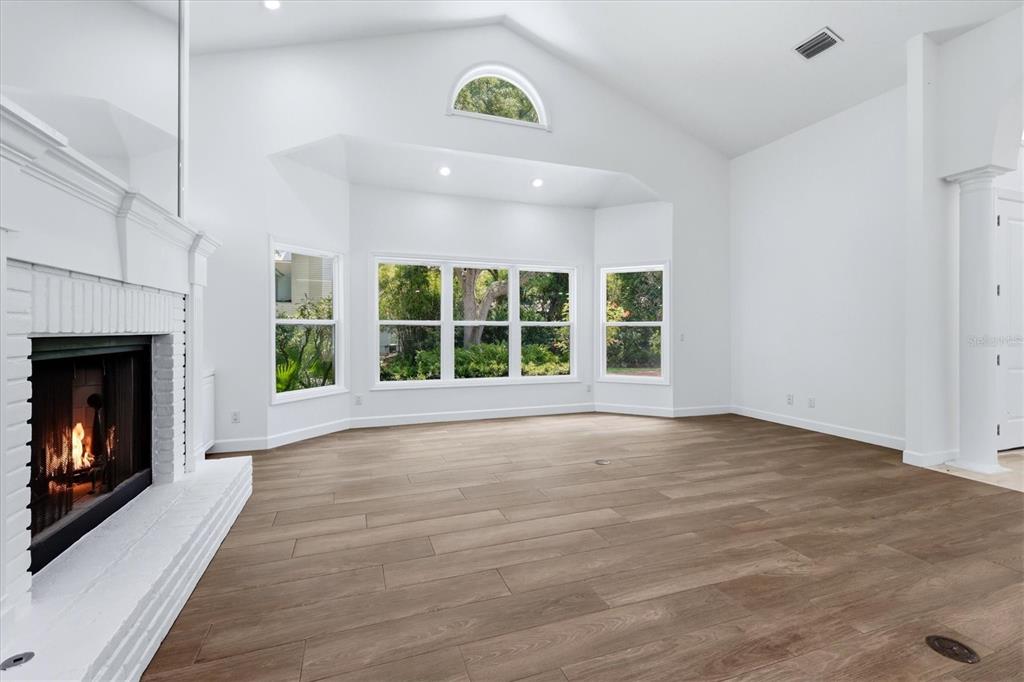 A bright living room features a white brick fireplace, vaulted ceilings, and wood-look tile flooring — 1351 DIXIE LEE LANE, SARASOTA, FL