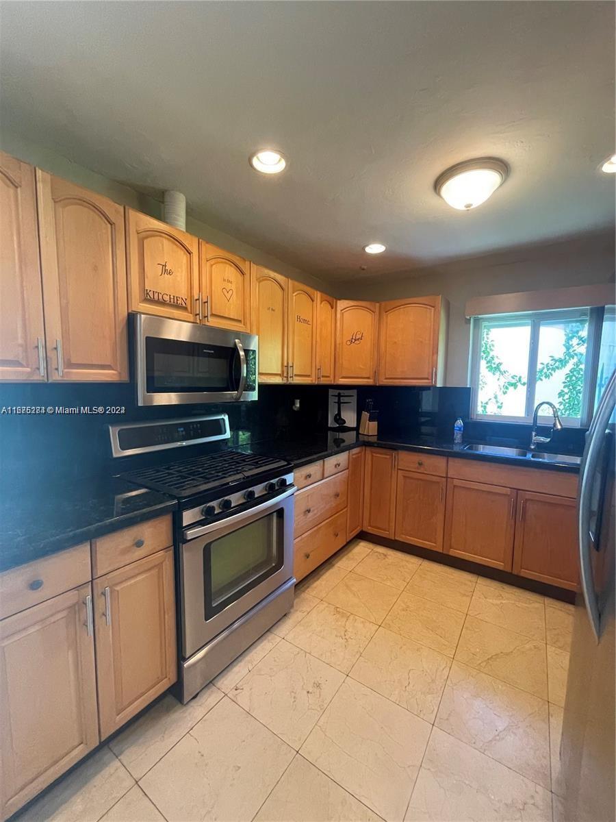 A kitchen features light wood cabinets, black countertops, stainless steel appliances, and beige tile flooring — 1531 Moffett St, Hollywood FL 33020, HOLLYWOOD, FL