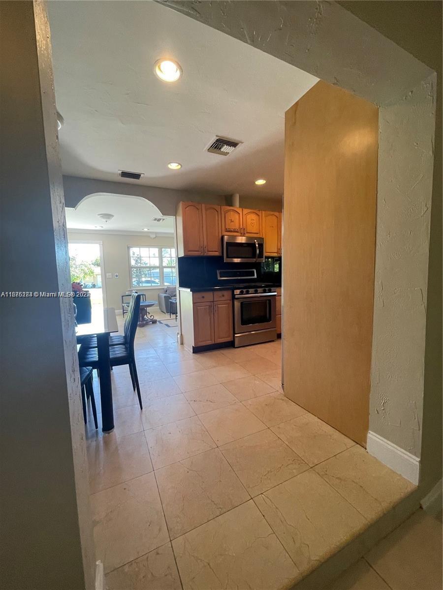 A tiled entryway leads into a kitchen with wood cabinets and stainless steel appliances — 1531 Moffett St, Hollywood FL 33020, HOLLYWOOD, FL