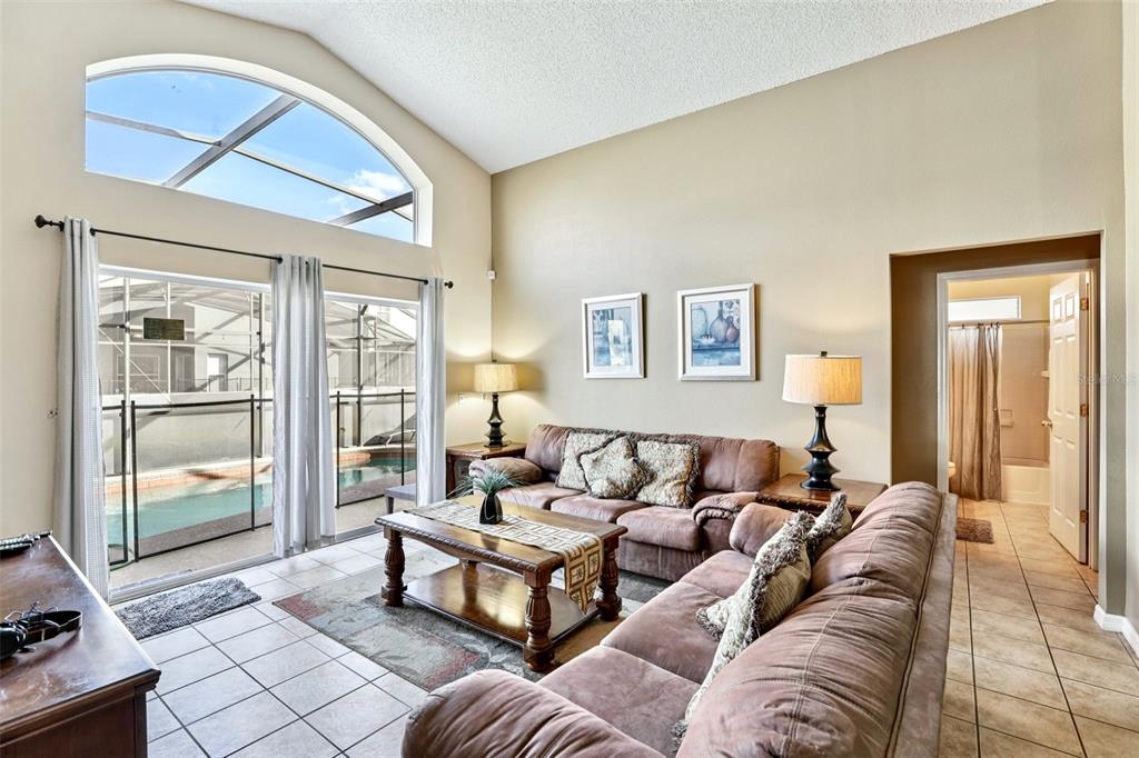 A living room with vaulted ceilings, tile floors, and sliding glass doors overlooking a pool — 151 HIDEAWAY BEACH LANE, KISSIMMEE, FL