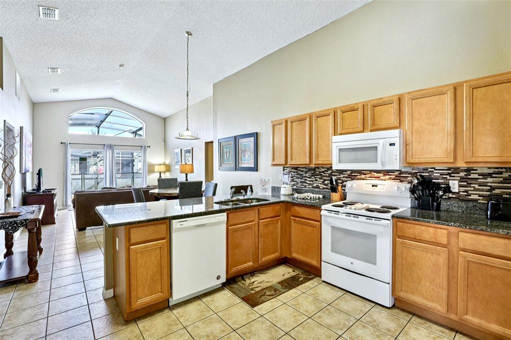 A kitchen with light wood cabinets, granite countertops, and a white stove overlooks a living area — 151 HIDEAWAY BEACH LANE, KISSIMMEE, FL
