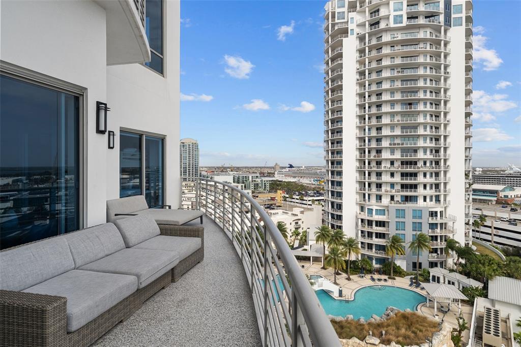 A curved balcony features gray outdoor furniture overlooking a high-rise building and a swimming pool — 449 S 12TH STREET UNIT 1402, TAMPA, FL