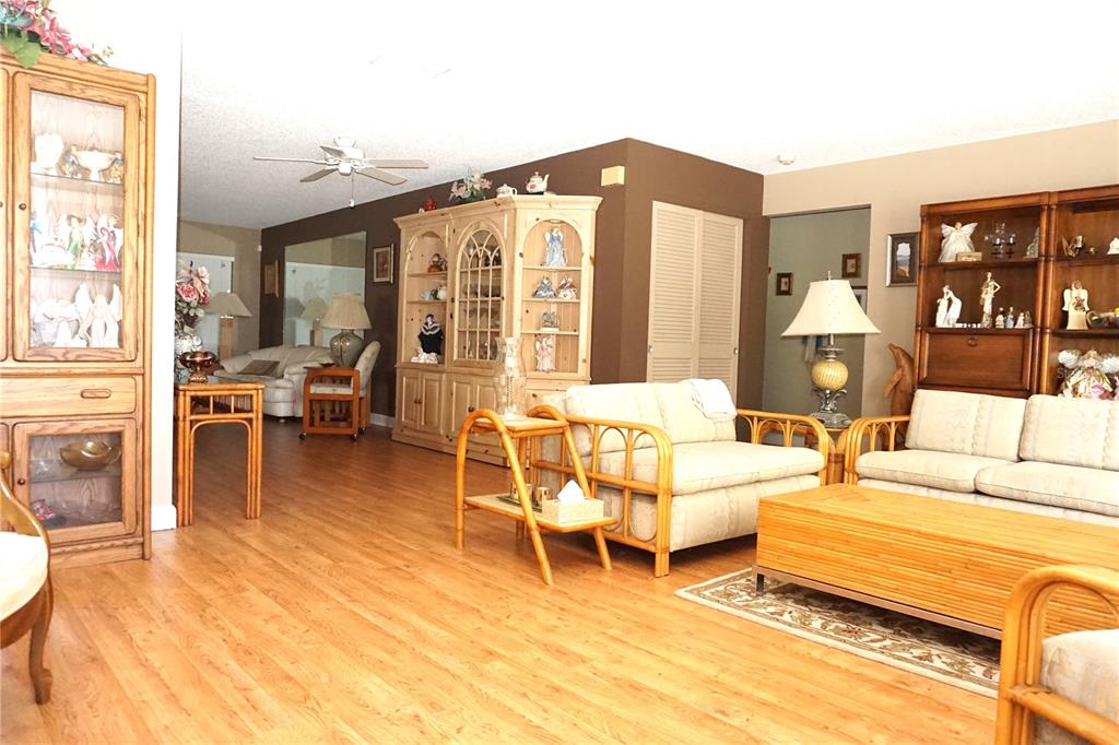A living room features light wood flooring, rattan furniture, and two large wooden display cabinets — 4031 93RD TERRACE N UNIT 5, PINELLAS PARK, FL