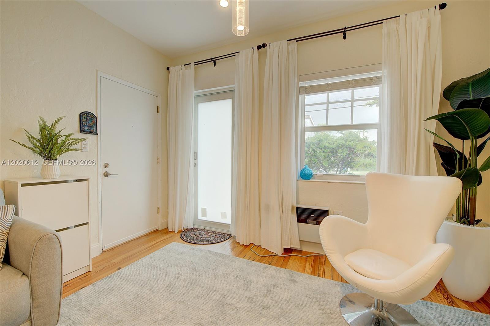 A living room features a white chair, a glass door, a window, and hardwood floors — 2463 Pine Tree Dr # 3, Miami Beach FL 33140, MIAMI BEACH, FL