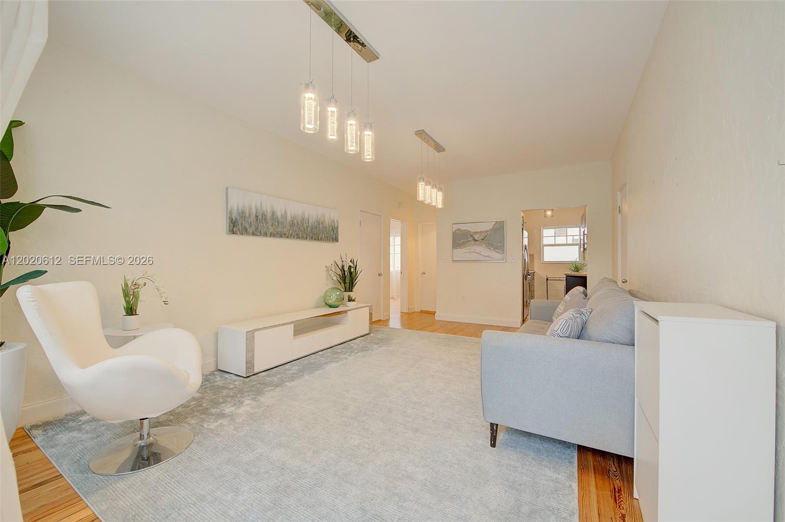 A living room features a white swivel chair, a light gray sofa, and modern pendant lighting — 2463 Pine Tree Dr # 3, Miami Beach FL 33140, MIAMI BEACH, FL