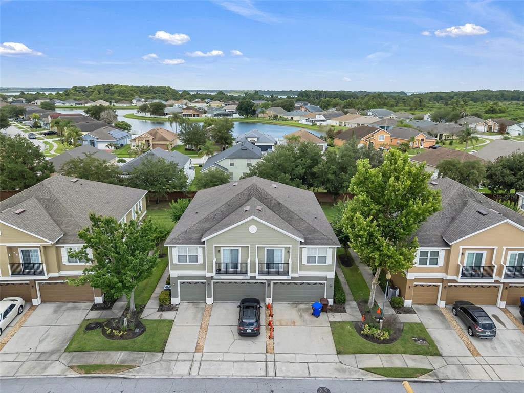 An aerial view shows three attached townhomes with driveways, garages, and balconies facing a lake — 1913 ESTANCIA CIRCLE UNIT 1913, KISSIMMEE, FL