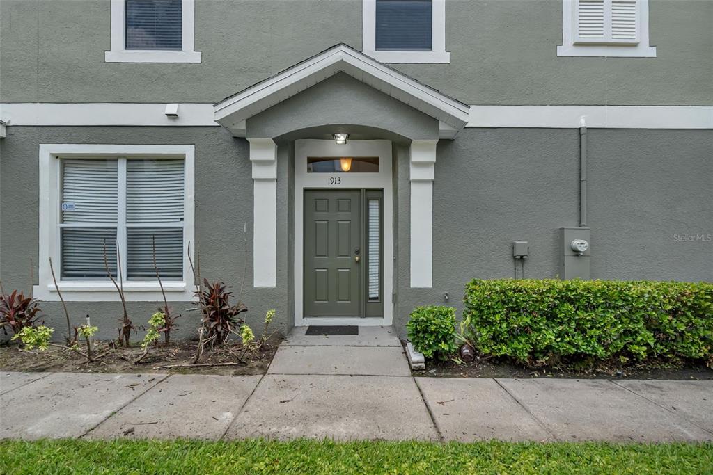 The exterior of a gray building features a green front door with a transom window — 1913 ESTANCIA CIRCLE UNIT 1913, KISSIMMEE, FL