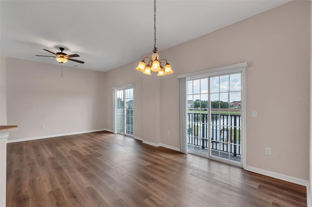 An empty room with wood-look flooring, a ceiling fan, a chandelier, and two sliding doors — 1913 ESTANCIA CIRCLE UNIT 1913, KISSIMMEE, FL