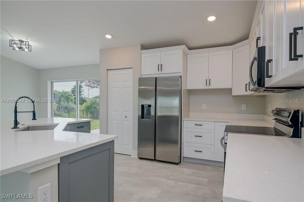 A modern kitchen features white cabinets, stainless steel appliances, and a gray kitchen island — 204 EL DORADO BLVD N, CAPE CORAL, FL