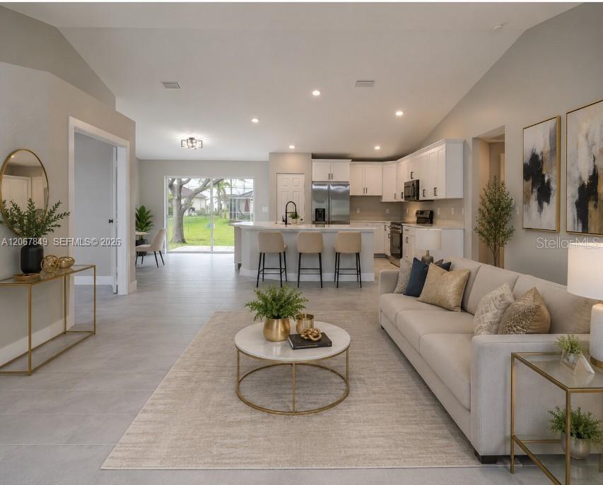 An open-concept living room and kitchen featuring white cabinetry, a breakfast bar, and tile flooring — 204 EL DORADO BLVD N, CAPE CORAL, FL