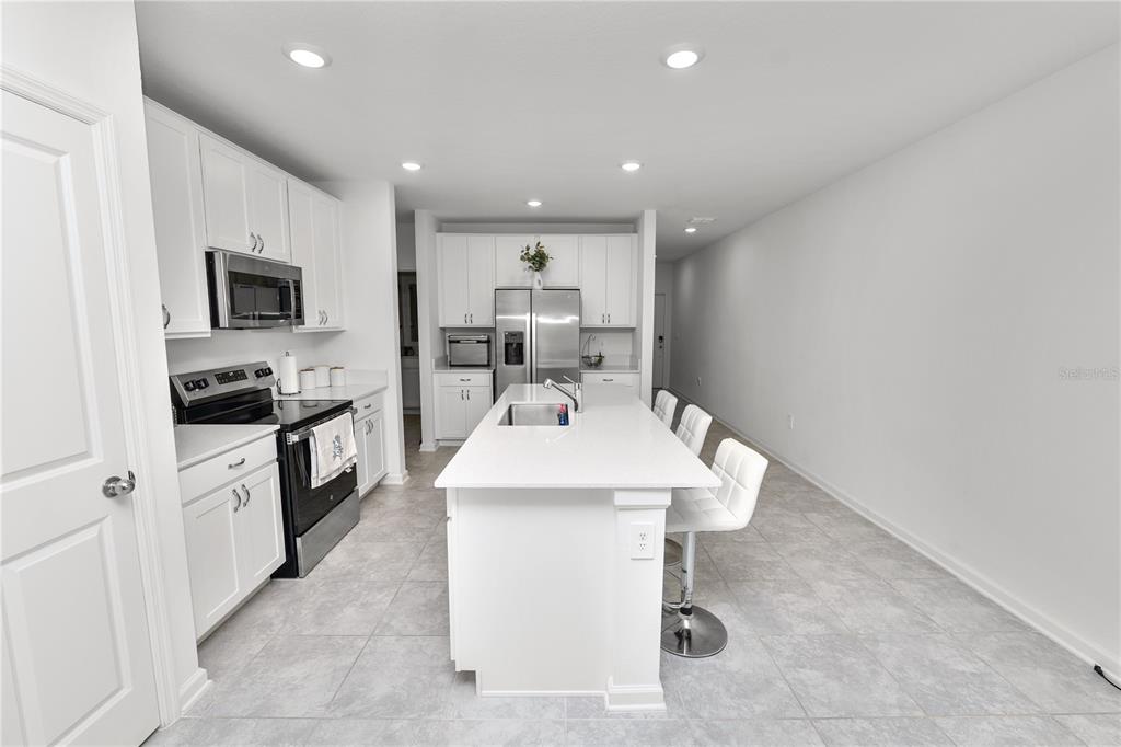 A modern kitchen features white cabinetry, stainless steel appliances, and a central island with seating — 1740 WHITE WATER COURT, DAVENPORT, FL