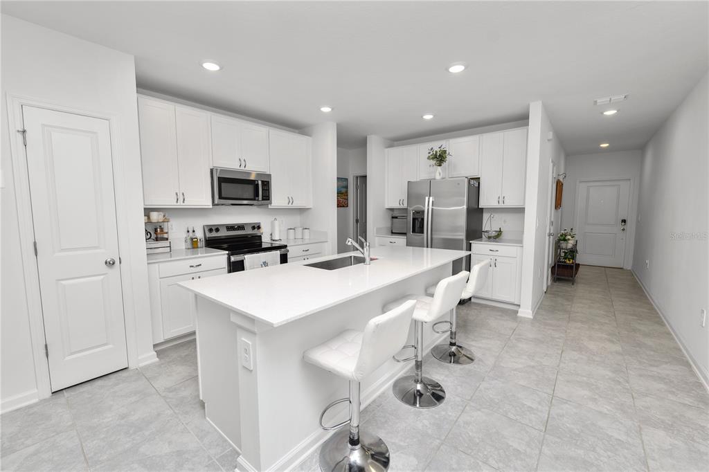 A modern kitchen features white cabinetry, a central island with bar seating, and stainless appliances — 1740 WHITE WATER COURT, DAVENPORT, FL