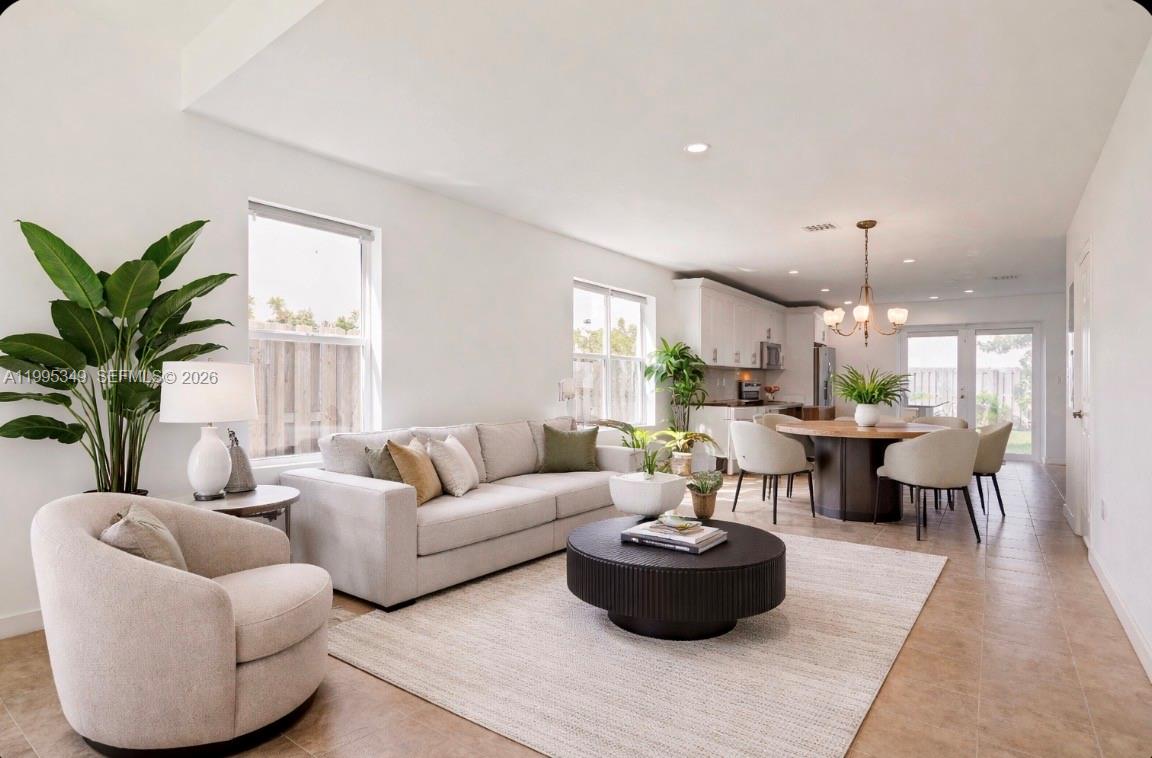 An open-concept living and dining area features tile flooring, neutral furniture, and a modern kitchen — 17970 SW 105th Ave, Miami FL 33157, MIAMI, FL