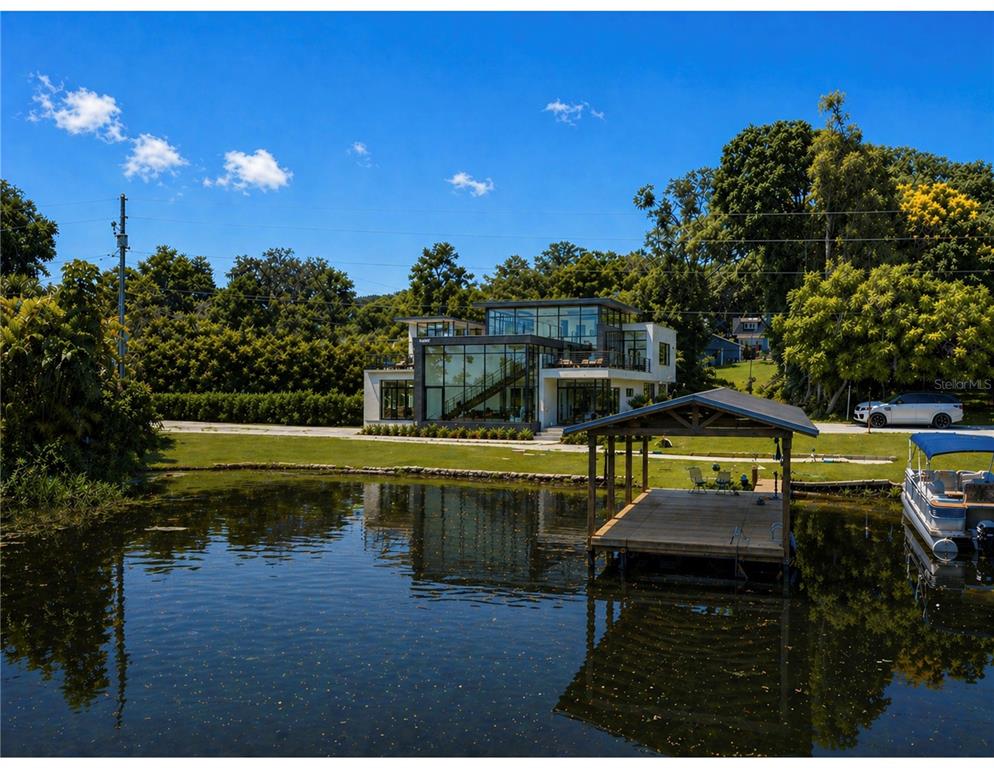 A modern glass-walled house sits beside a lake with a wooden boat dock — 212 W 1ST AVENUE, WINDERMERE, FL