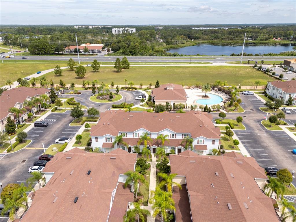 An aerial view shows multi-story residential buildings with brown roofs, parking lots, and a pool — 9008 SHINE DRIVE, KISSIMMEE, FL