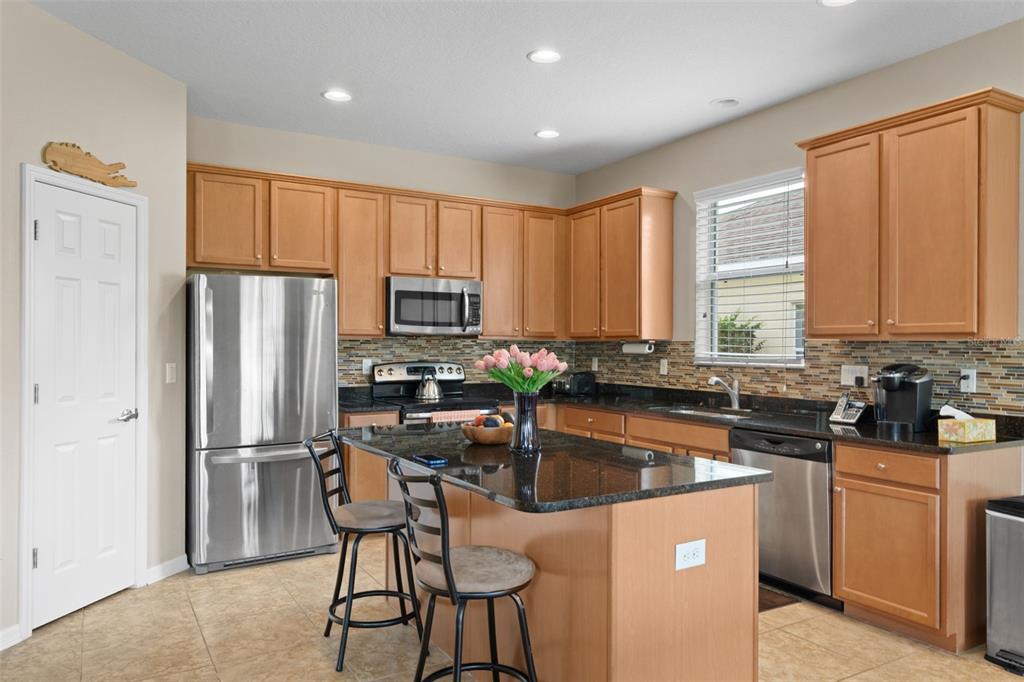 A kitchen features light wood cabinets, granite countertops, stainless steel appliances, and a central island — 11059 BELLE HAVEN DRIVE, NEW PORT RICHEY, FL