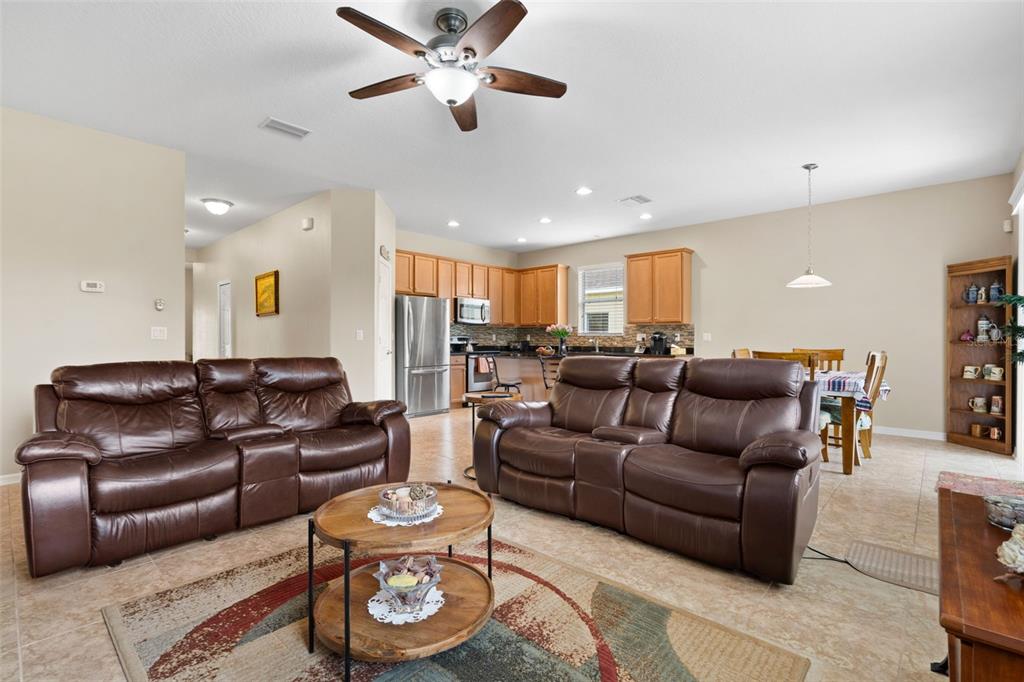 A living room with two brown leather sofas, a round coffee table, and an open kitchen — 11059 BELLE HAVEN DRIVE, NEW PORT RICHEY, FL