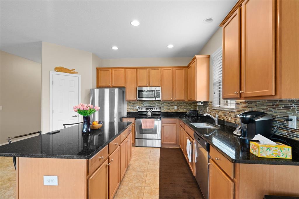 A kitchen features light wood cabinets, black granite countertops, stainless steel appliances, and a central island — 11059 BELLE HAVEN DRIVE, NEW PORT RICHEY, FL