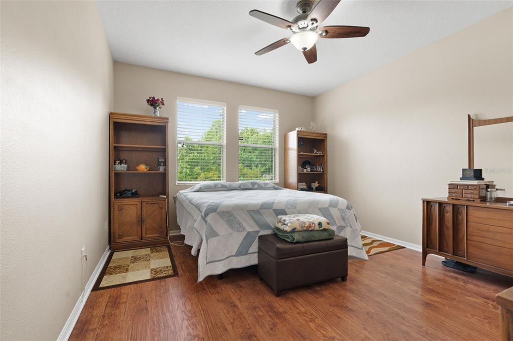 A bedroom features wood-look flooring, a ceiling fan, two windows, and wooden furniture — 11059 BELLE HAVEN DRIVE, NEW PORT RICHEY, FL