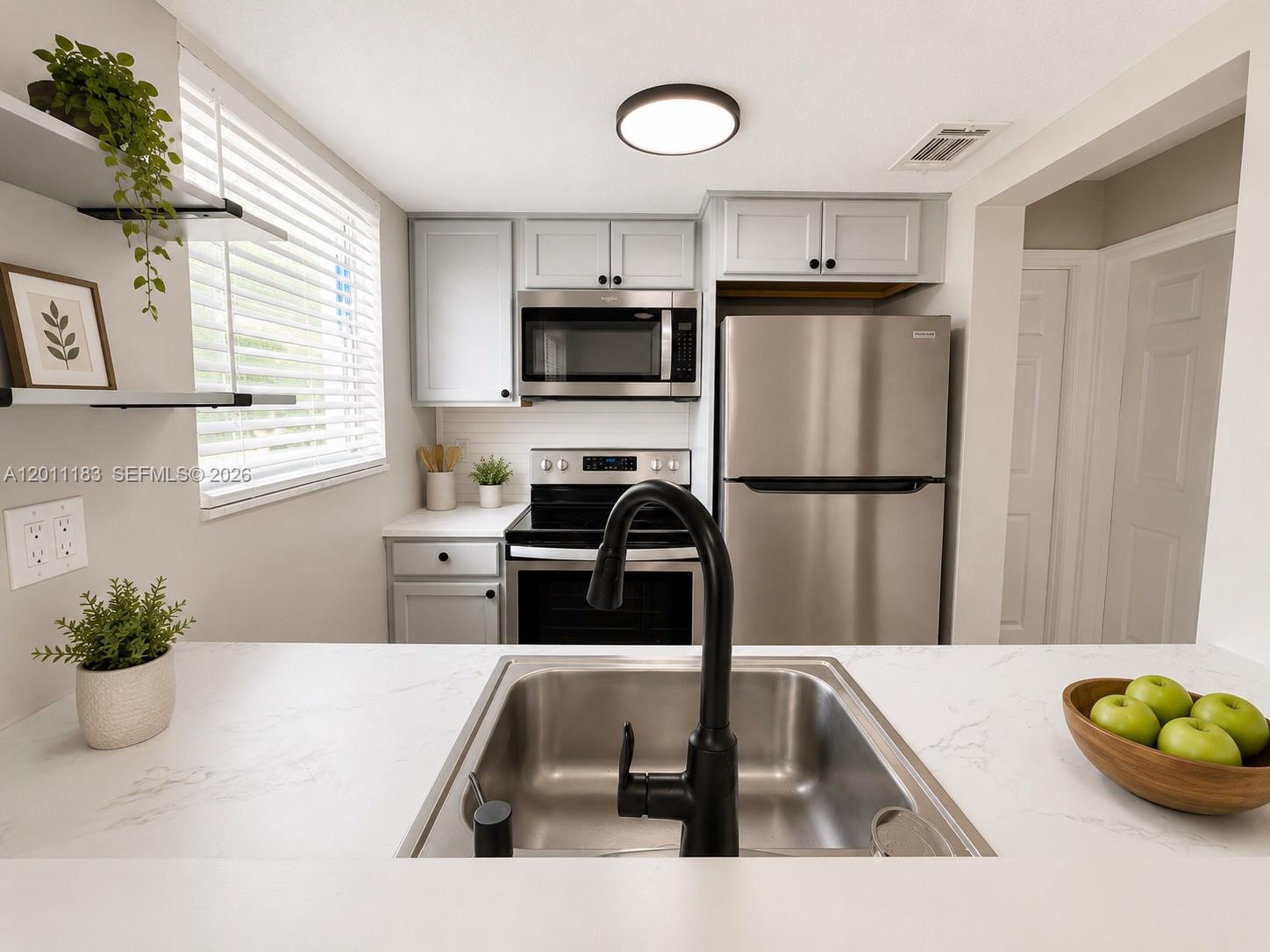 A kitchen features stainless steel appliances, light gray cabinets, and a white marble-look countertop — 1208 S Ridgewood Ave, Daytona FL 32114, DAYTONA, FL