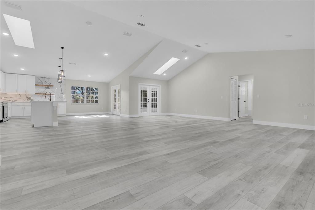 A spacious, open-concept living area features light wood-look flooring, vaulted ceilings, and a modern kitchen — 1812 COROLLA COURT, DELTONA, FL