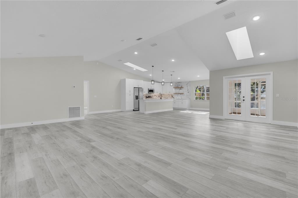 A spacious, open-concept living area features light gray wood-look flooring, vaulted ceilings with skylights, and a kitchen — 1812 COROLLA COURT, DELTONA, FL