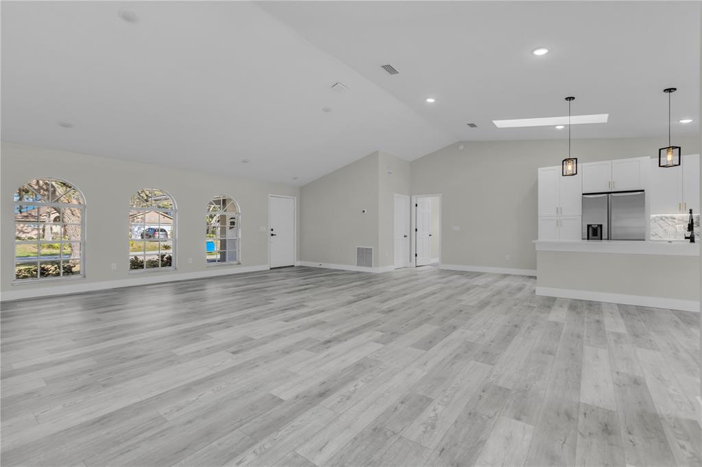 A spacious living area with light wood-look flooring, vaulted ceilings, and an open kitchen — 1812 COROLLA COURT, DELTONA, FL
