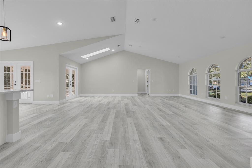 A spacious living room features vaulted ceilings, light wood-look flooring, and three arched windows — 1812 COROLLA COURT, DELTONA, FL