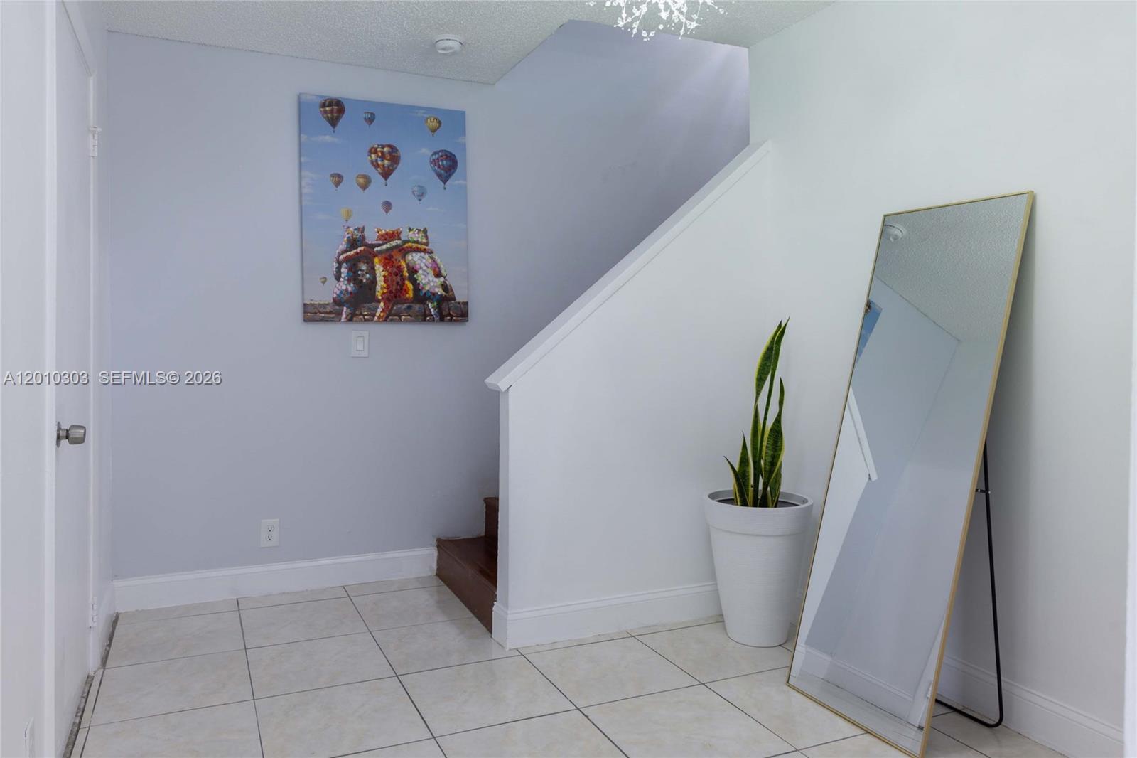 An entryway features light-colored tile flooring, a staircase, a floor mirror, and wall art — 9470 Atlantic St, Miramar FL 33025, MIRAMAR, FL