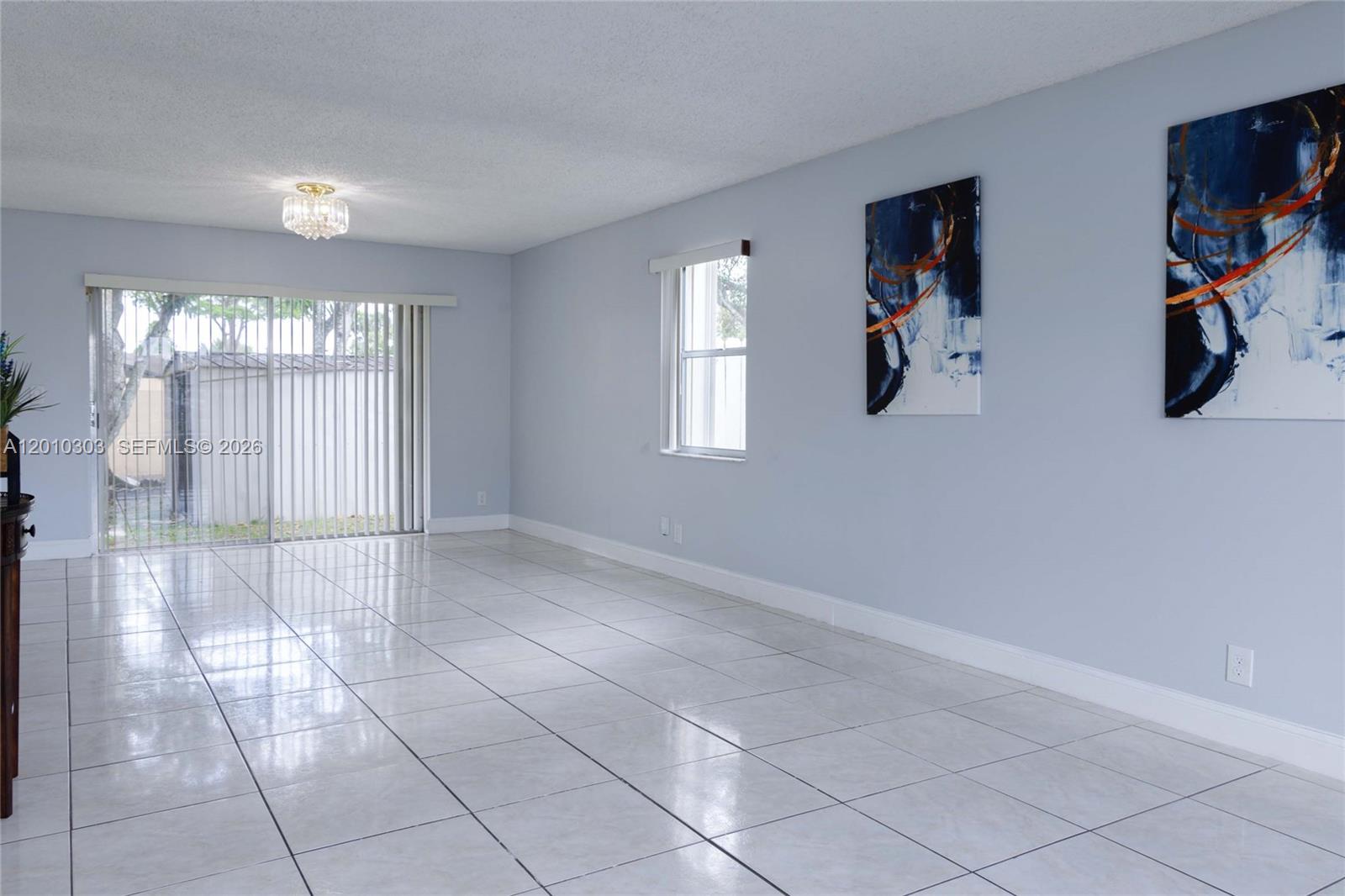 A bright living room features light blue walls, white tile flooring, and two abstract paintings — 9470 Atlantic St, Miramar FL 33025, MIRAMAR, FL