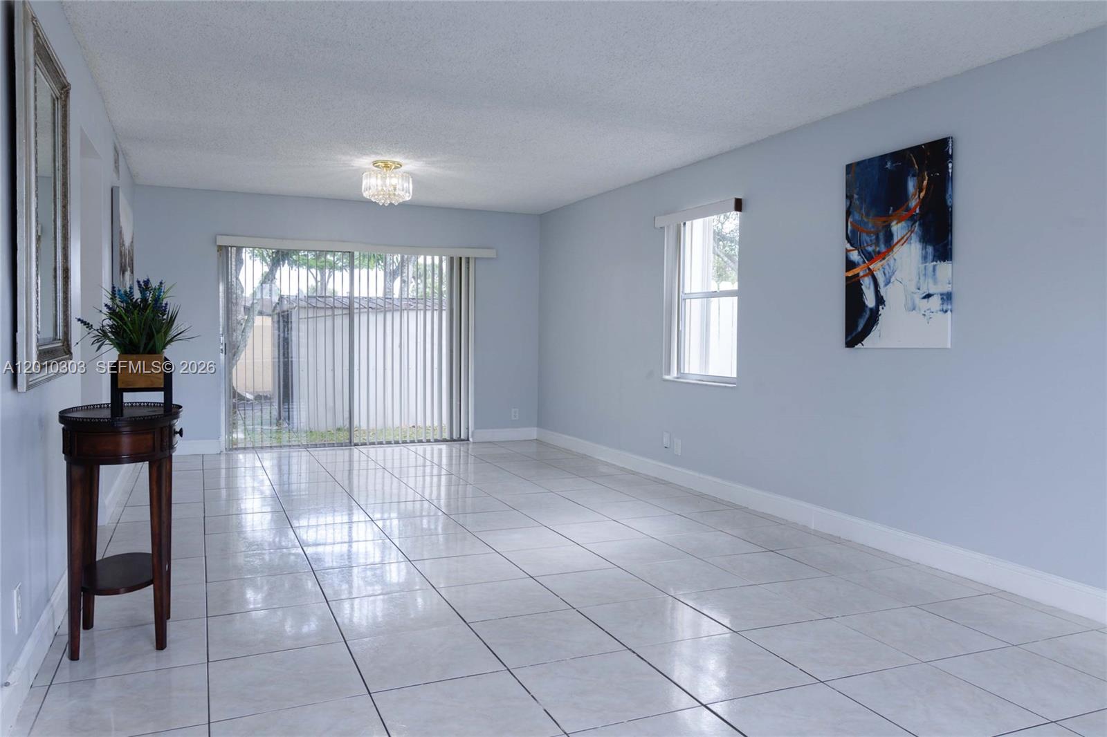 A living room features light blue walls, white tile flooring, a chandelier, and sliding glass doors — 9470 Atlantic St, Miramar FL 33025, MIRAMAR, FL
